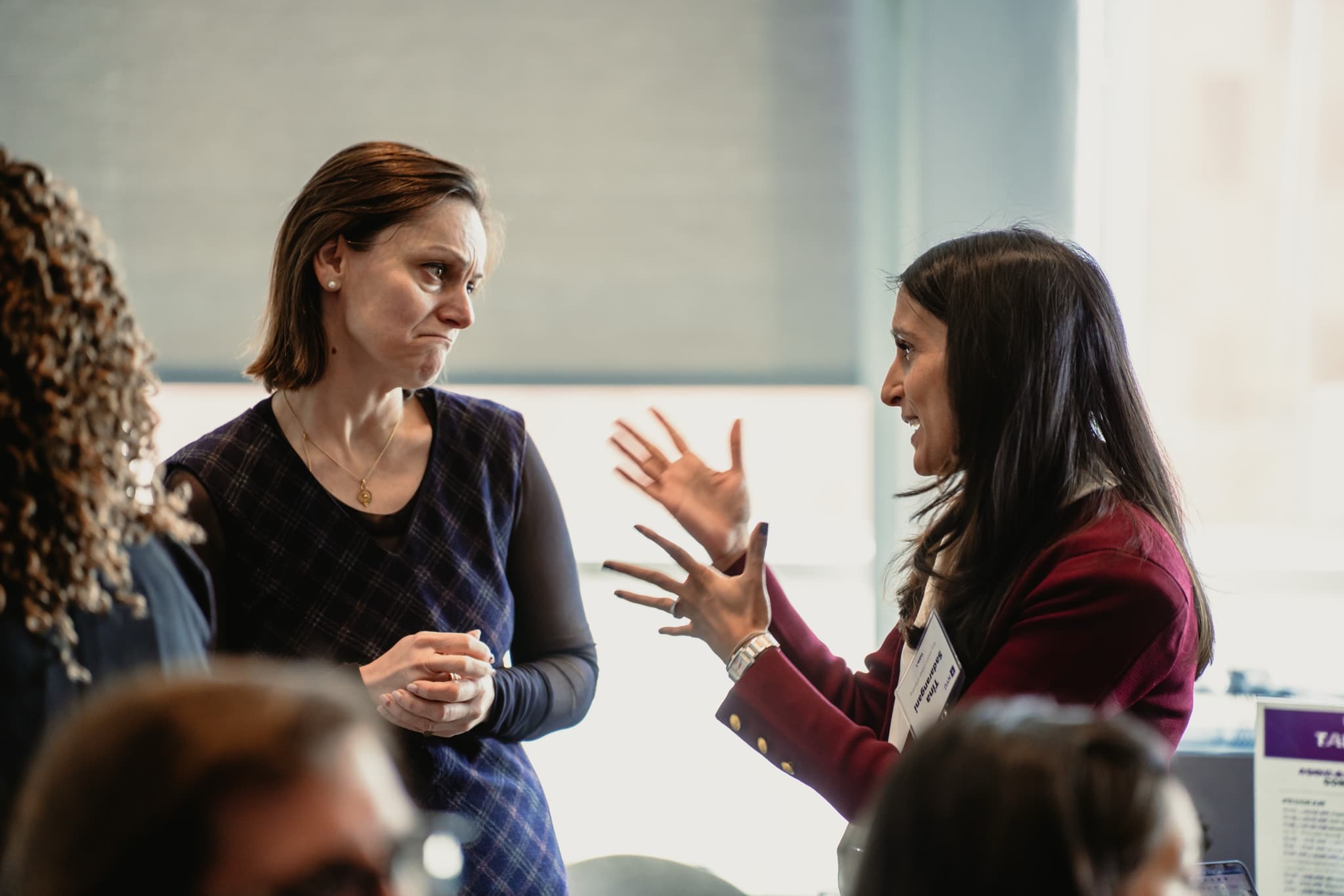 Dr. Tina Sadarangani in conversation with another woman at a professional event, both hands raised mid-sentence